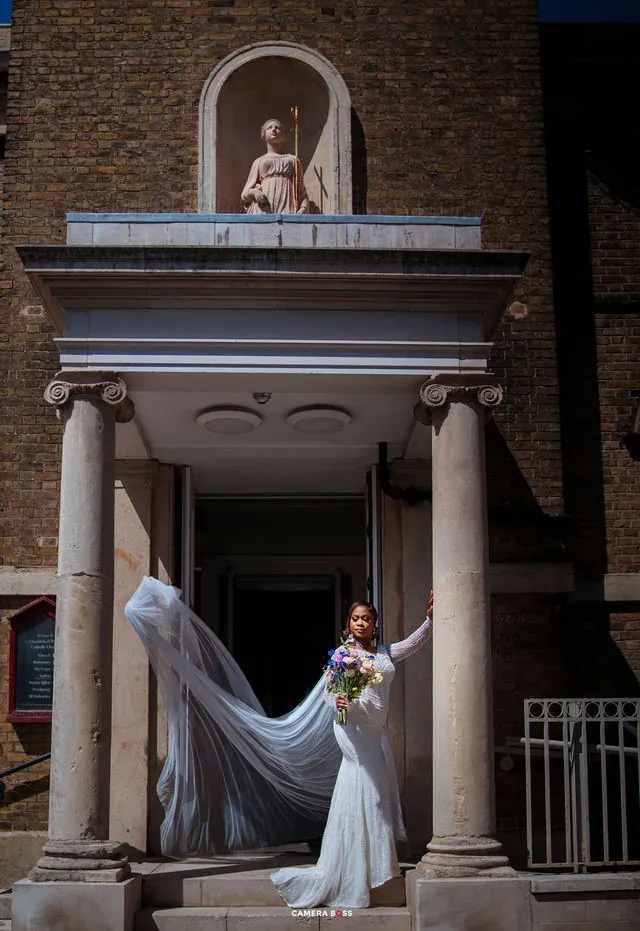 The bride lifting her veil outside a columned entrance. CameraBoss portfolio: Cynthia and Oswaldo.