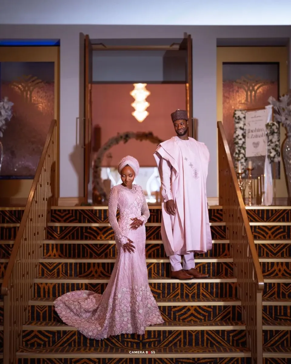 A couple in coordinated pink attire pose on a rustic wooden balcony with romantic lighting.
