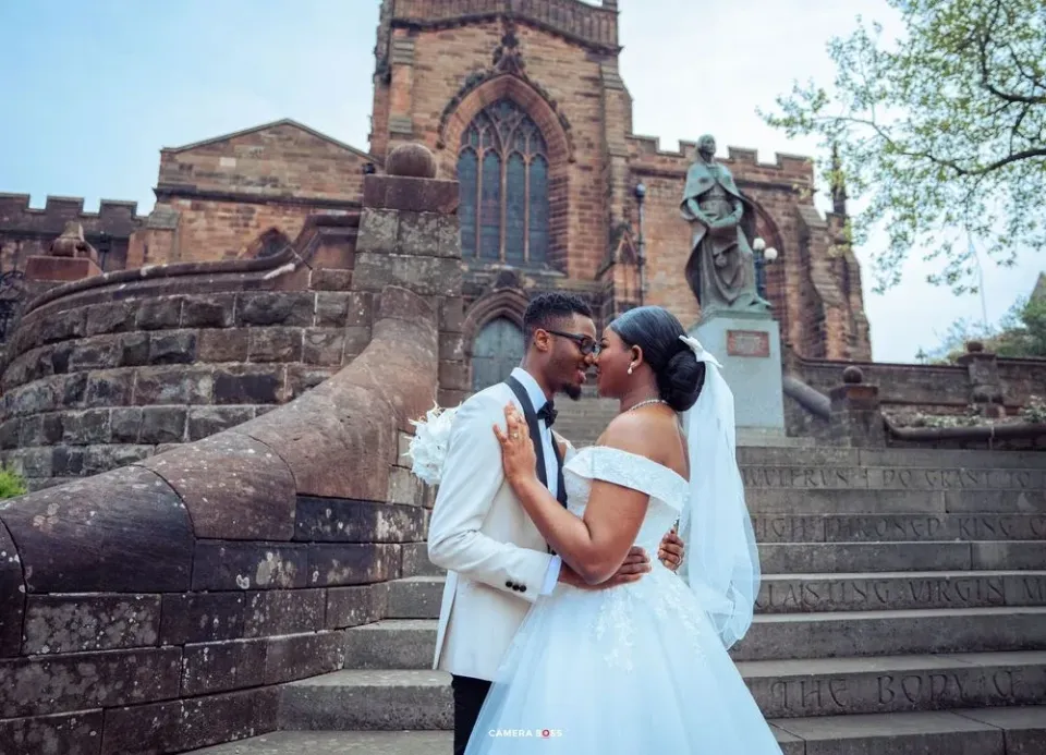 A couple embraces on stone church steps during their wedding photoshoot against gothic architectural backdrop.